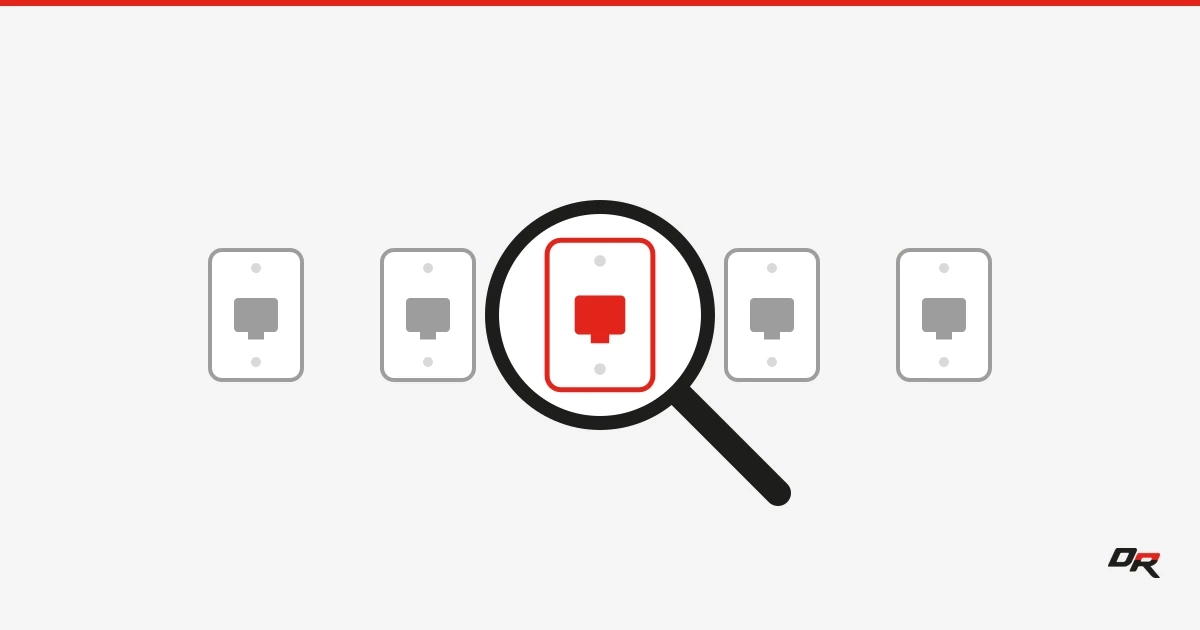 Five gray wall-jack faceplates in a row on an off-white background, with a black magnifying glass held over the center plate, which shows red inside the lens.